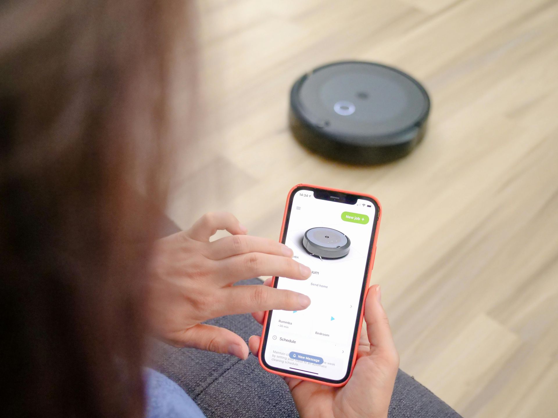 Person using a smartphone to control a robot vacuum on a wooden floor.