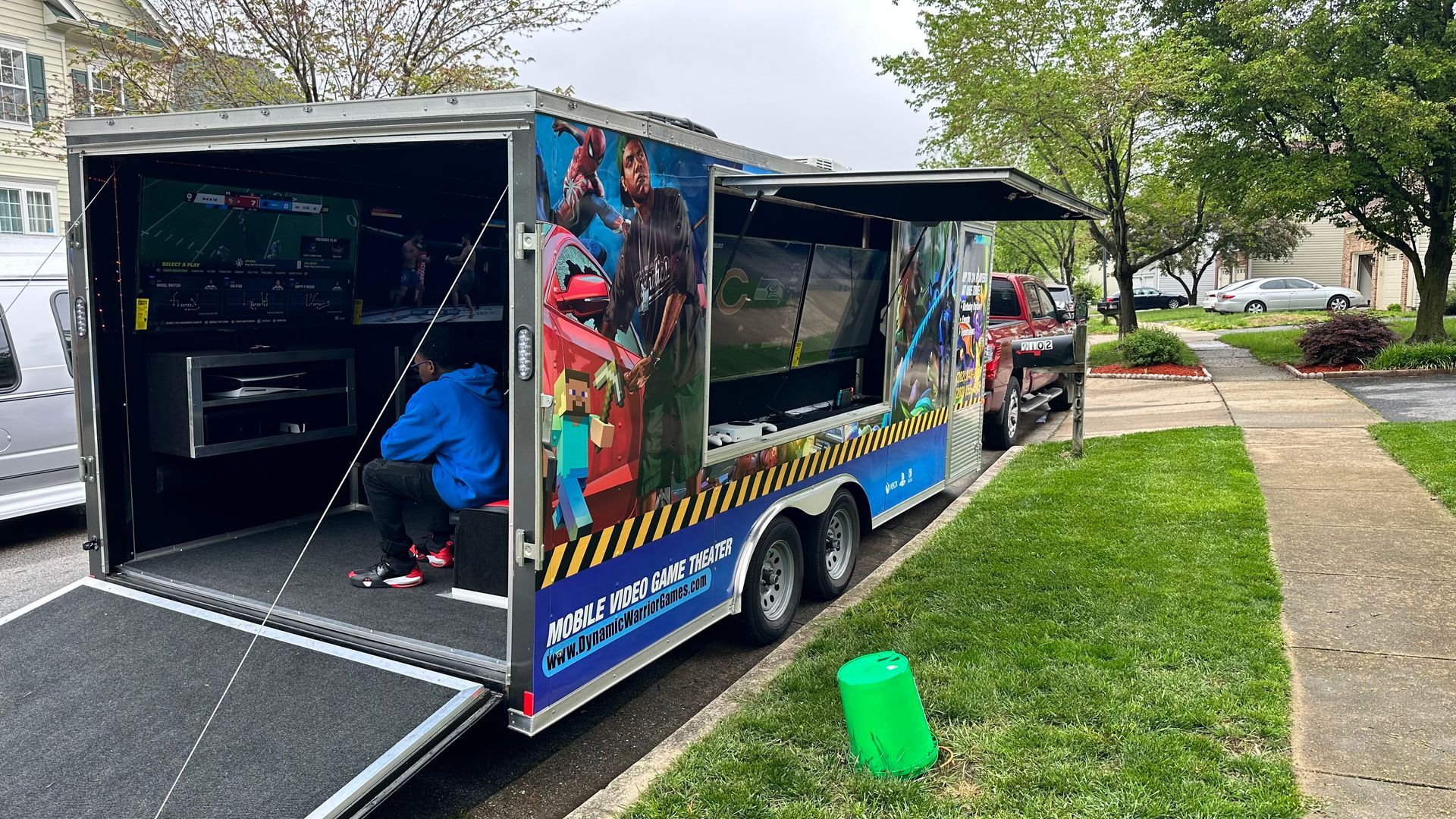 Gaming trailer parked on grass with person inside playing games. Side door open.