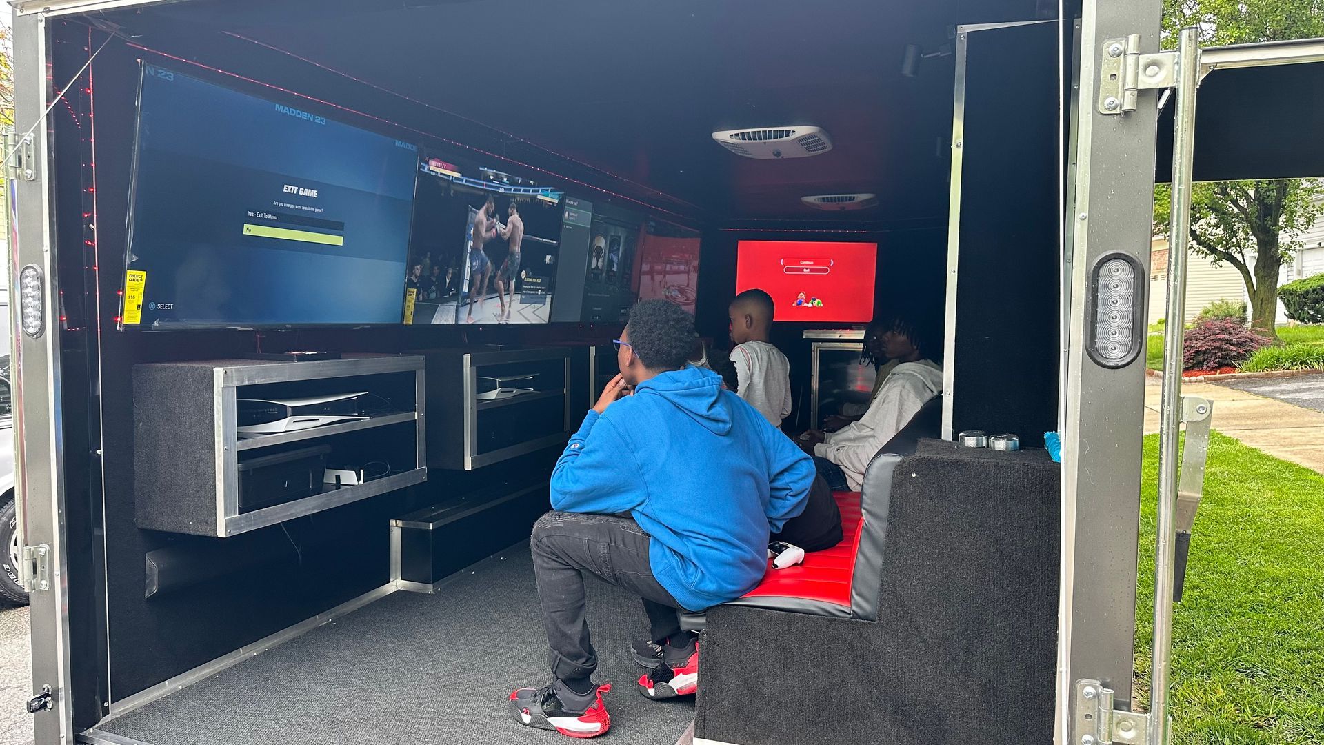 Kids playing video games inside a mobile gaming trailer with multiple screens.