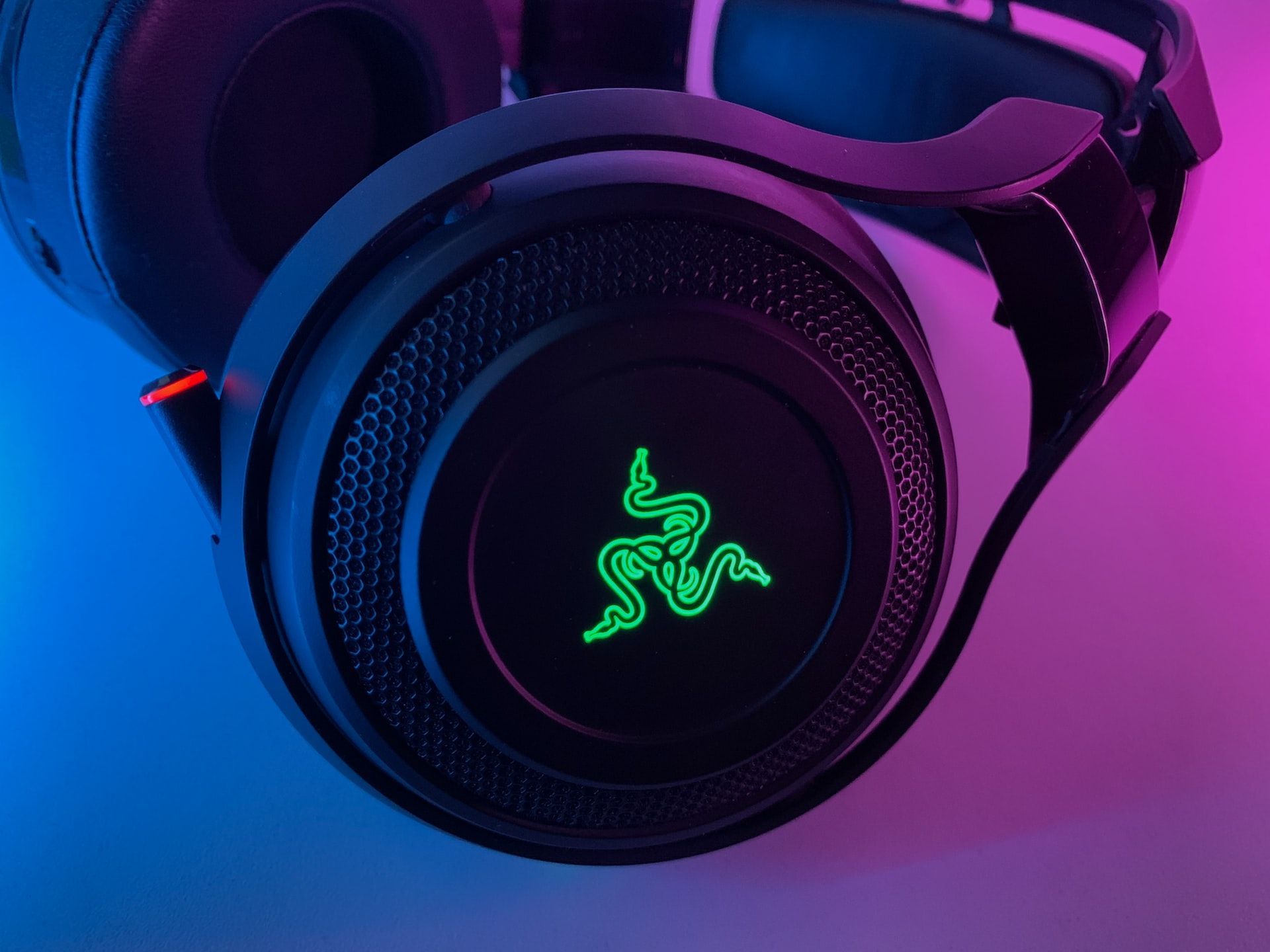 Black Razer gaming headset with glowing green logo, illuminated by blue and pink light.