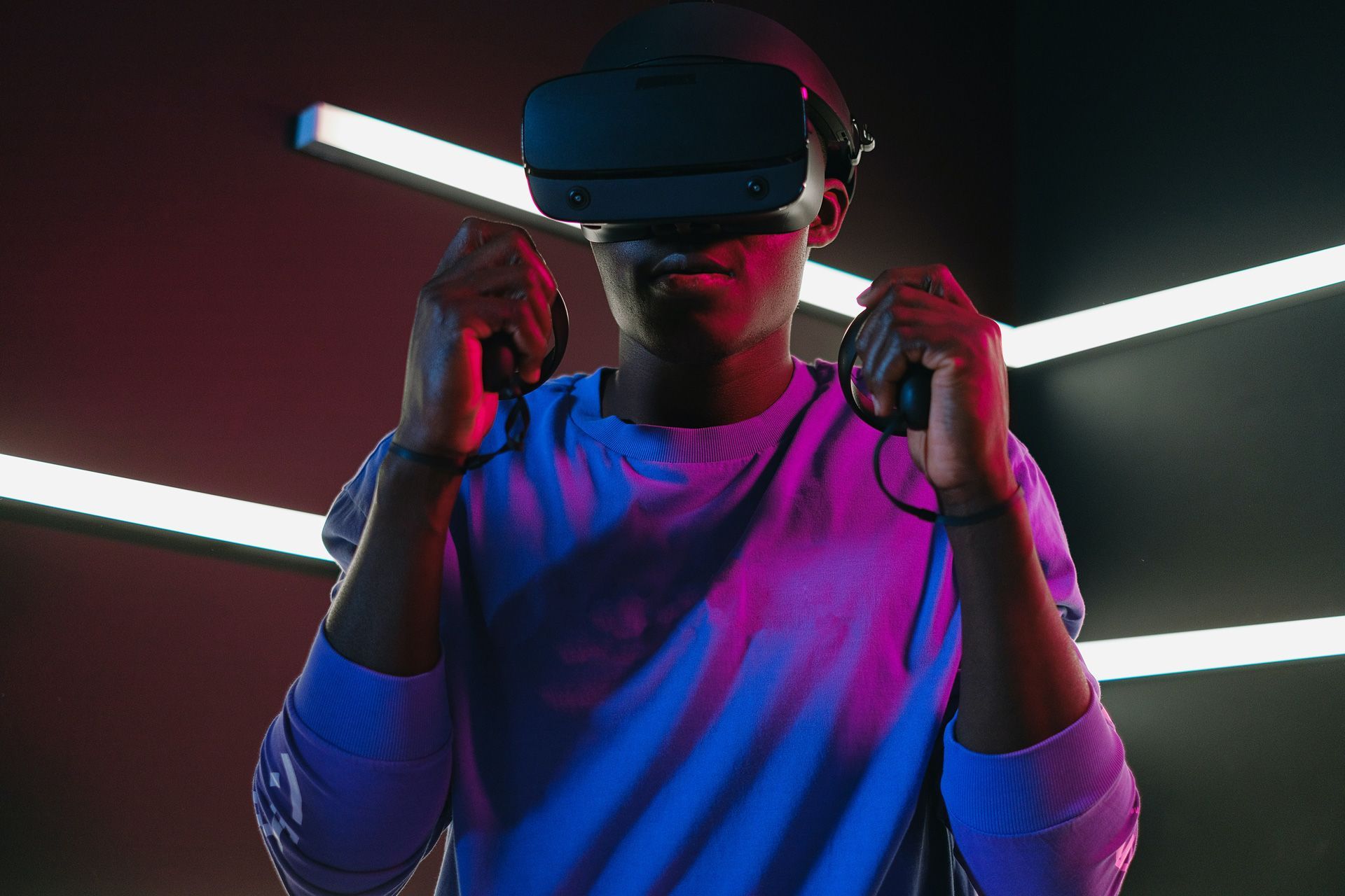 Person wearing VR headset and controllers, surrounded by blue and pink neon lights.