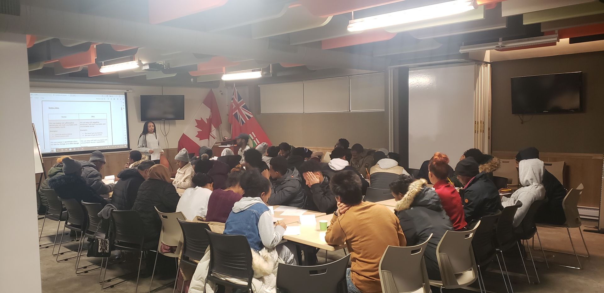 A group of people seated around tables in a room with a presentation screen and Canadian flags.