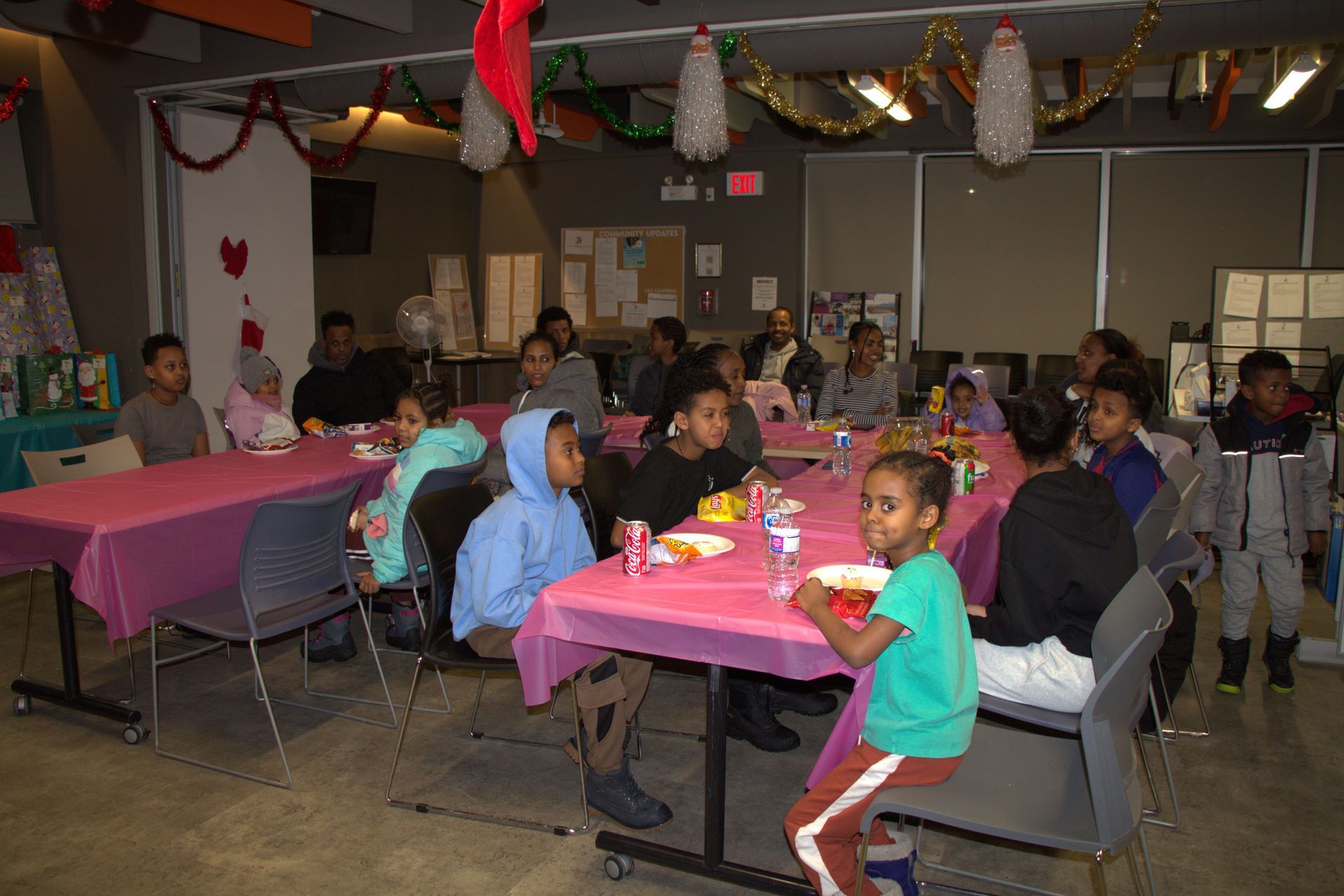 Children seated at pink tables, gathered for a party with decorations.