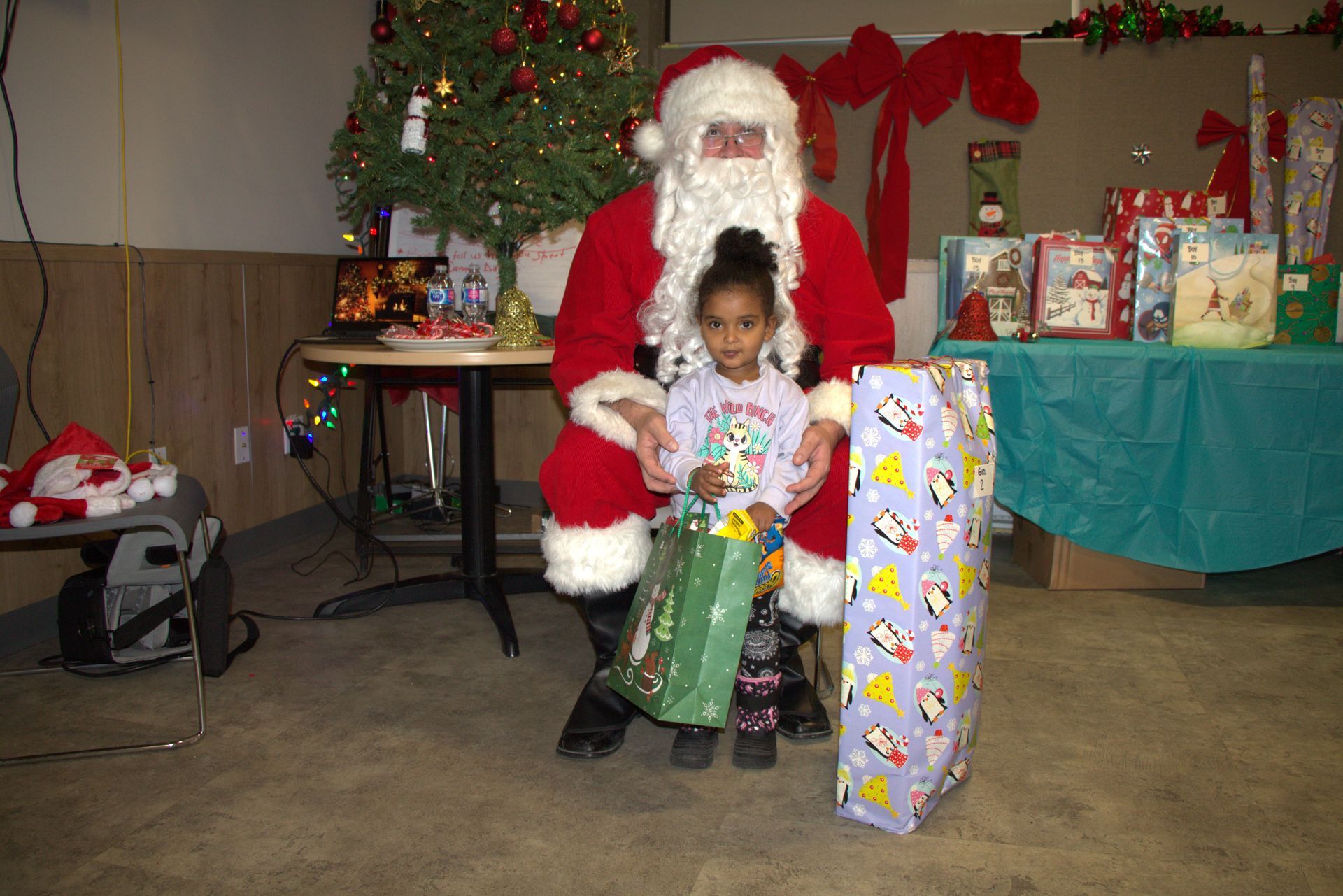 Santa Claus with a child holding gifts in front of a Christmas tree.