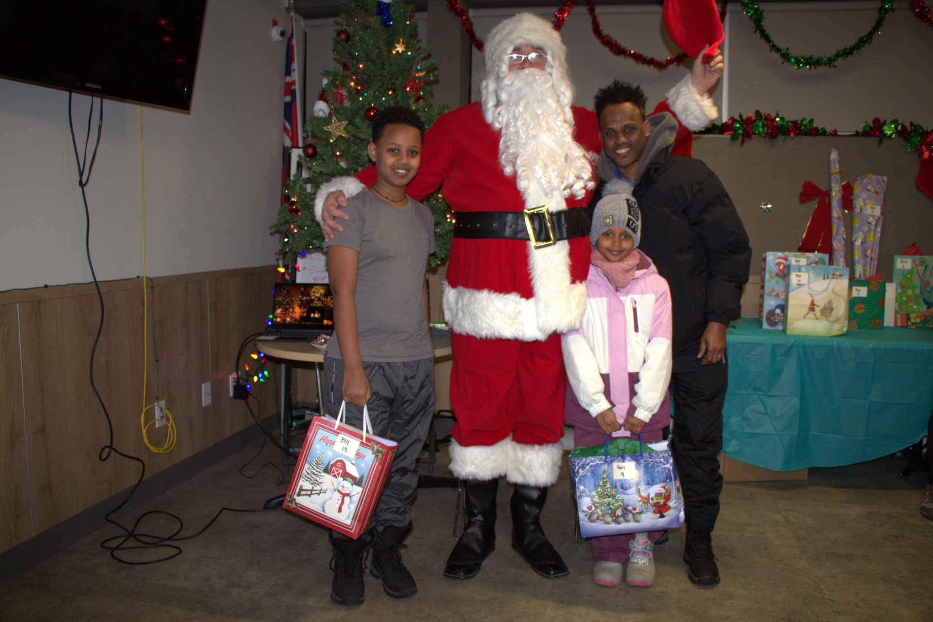 Santa Claus with two children and an adult; Christmas setting with gifts and tree.