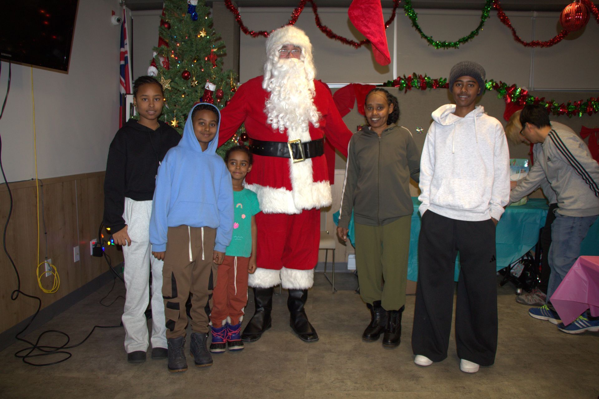 Santa Claus poses with a group of children in front of a Christmas tree.