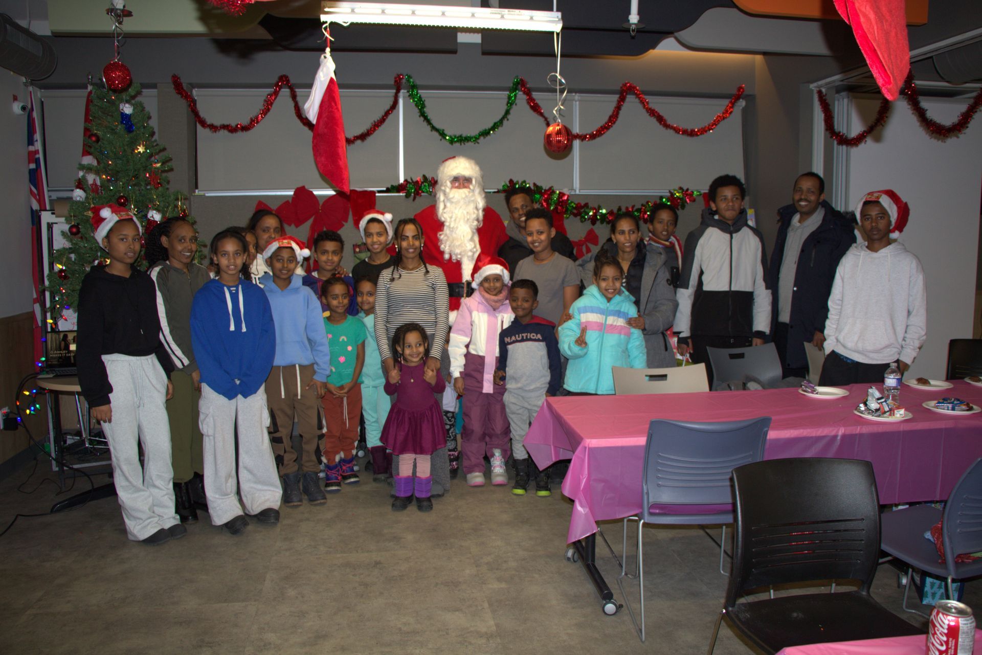 Santa Claus with a group of people, festive decorations, Christmas tree, pink tablecloth.