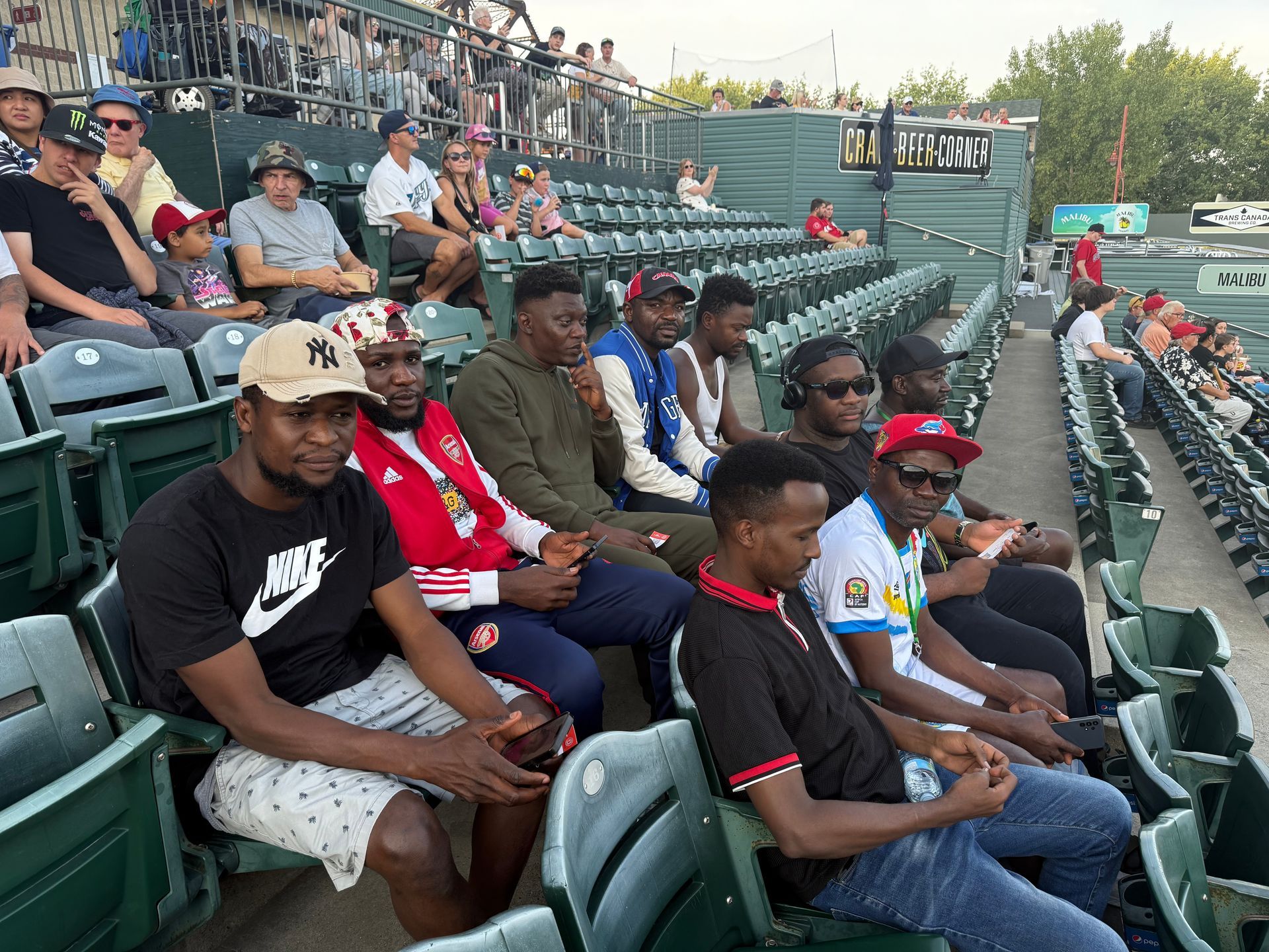 People seated in stadium bleachers, watching a game. Some wear hats, looking forward.