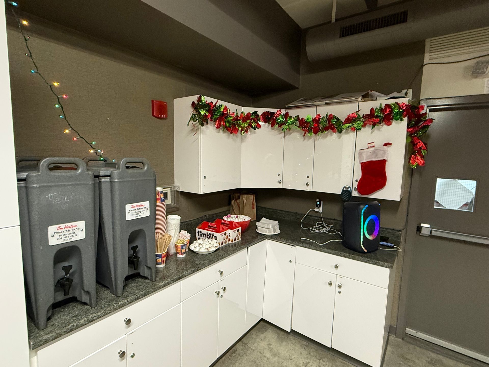 Coffee station in a corner, decorated for Christmas with garland, a stocking, and treats.
