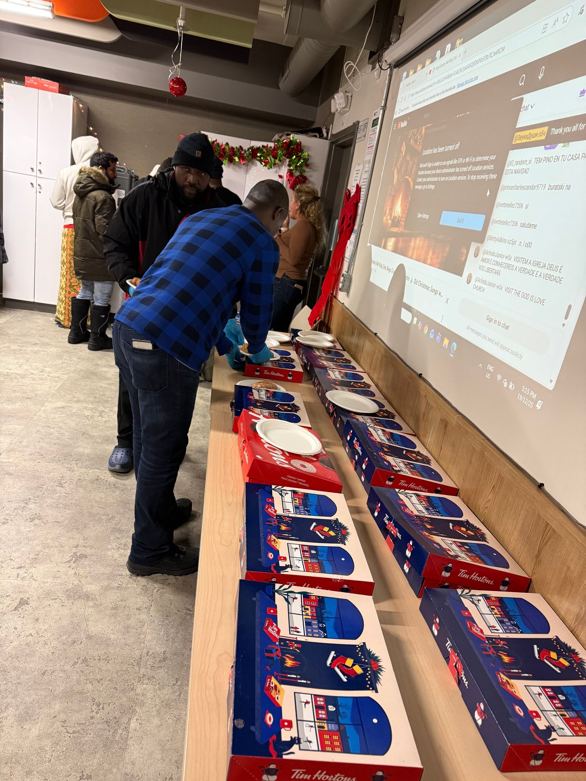 People looking at boxed gifts on a long table in a room, a projector screen visible in the background.