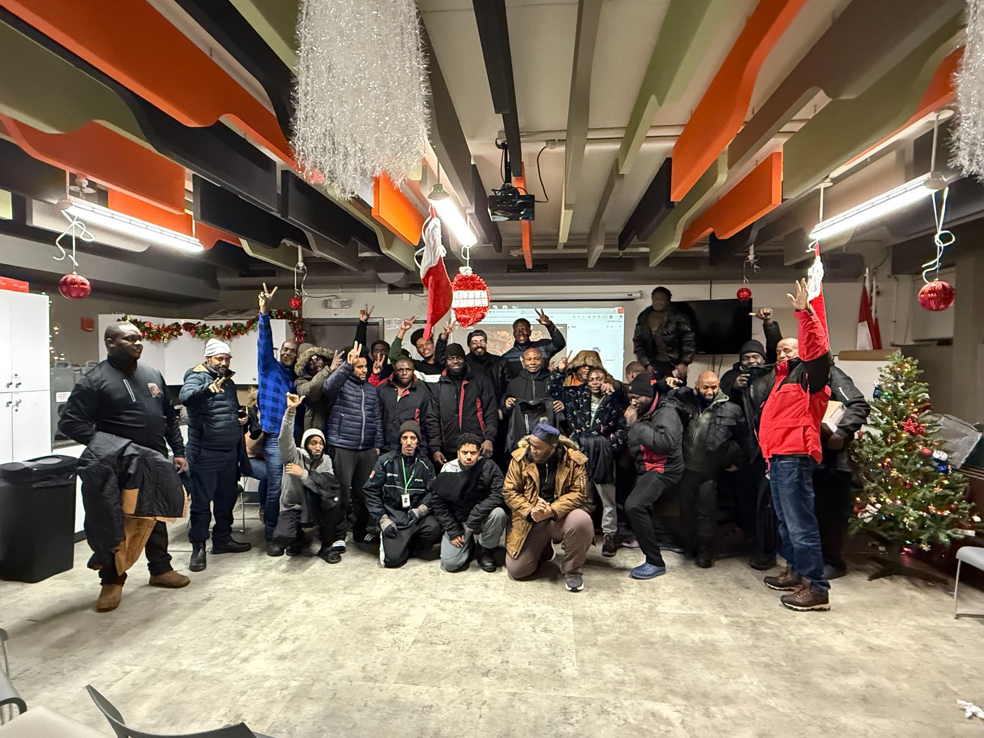 Group of people celebrating in a room with Christmas decorations. Some are raising their arms with cheerful expressions.