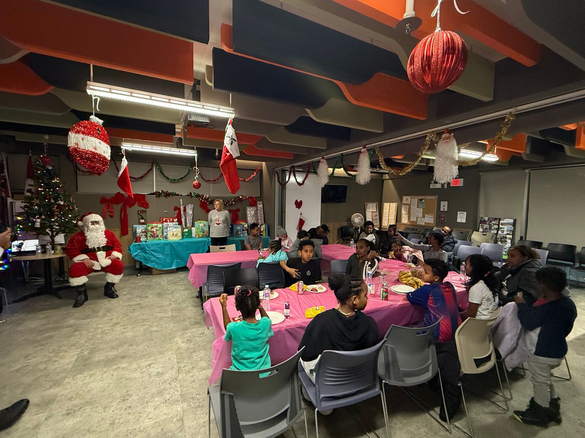 Children seated at tables, Santa Claus with gifts, decorated room, Christmas party.