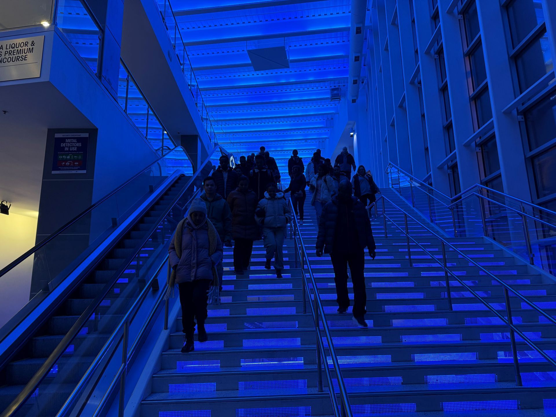 People ascend illuminated blue stairs inside a building.