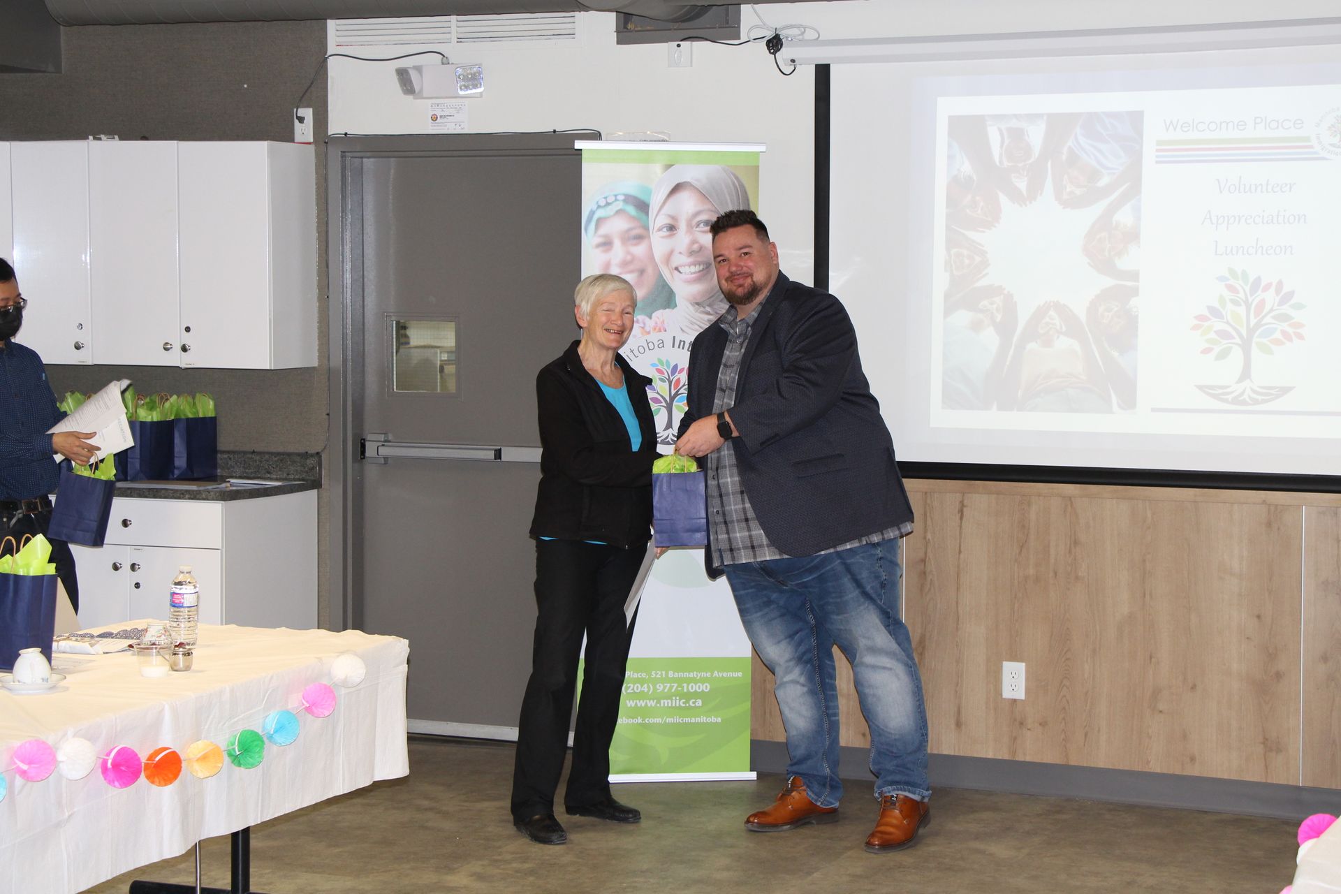 A man is giving a woman a gift in front of a projector screen.