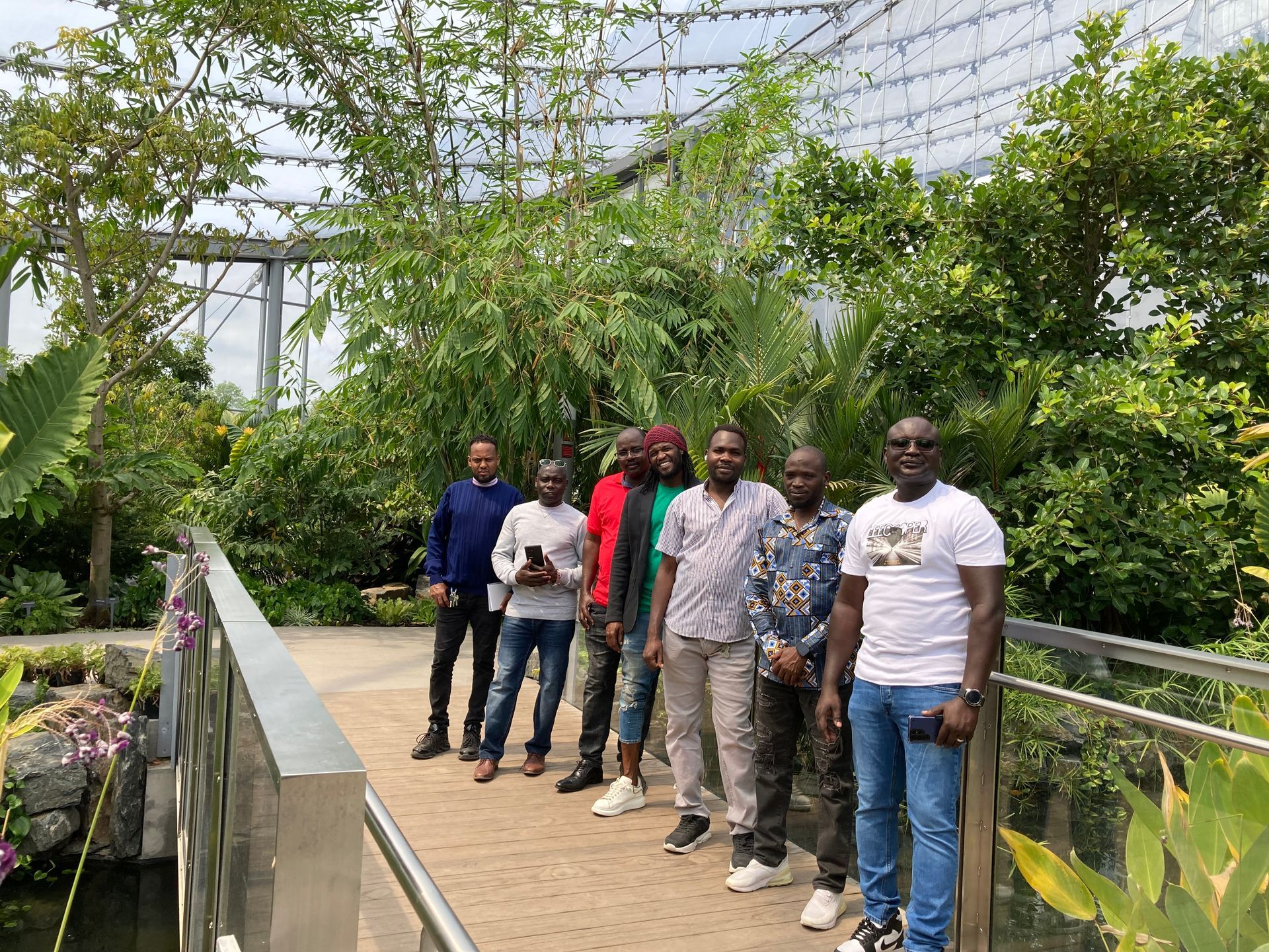 Five people standing on a garden walkway in a lush greenhouse with hanging plants