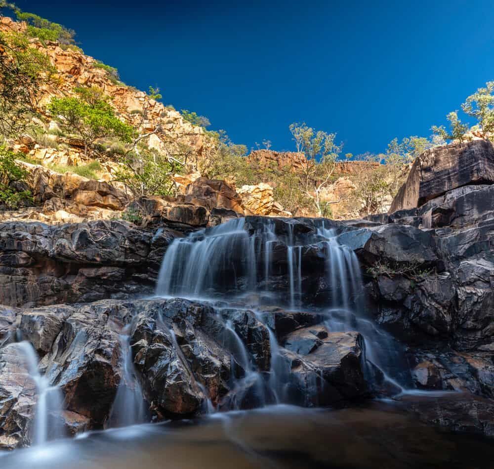 A Waterfall Surrounded by Rocks and Trees With a Blue Sky in the Background — East-West Fire Services In Cloncurry, QLD