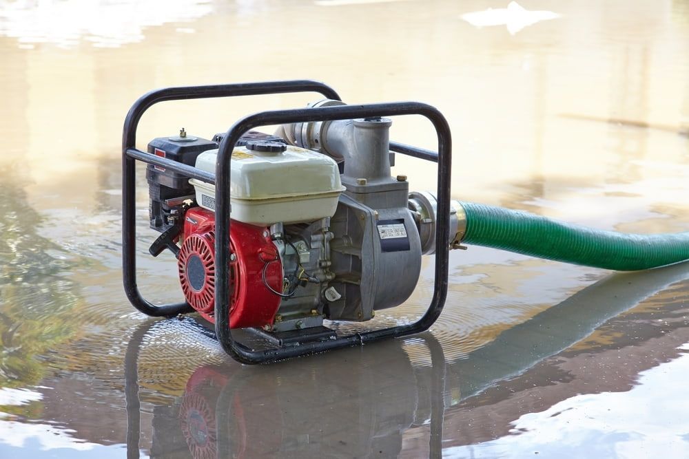 A Water Pump With a Green Hose Attached to It is Sitting in a Puddle of Water — East-West Fire Services In Airlie Beach, QLD