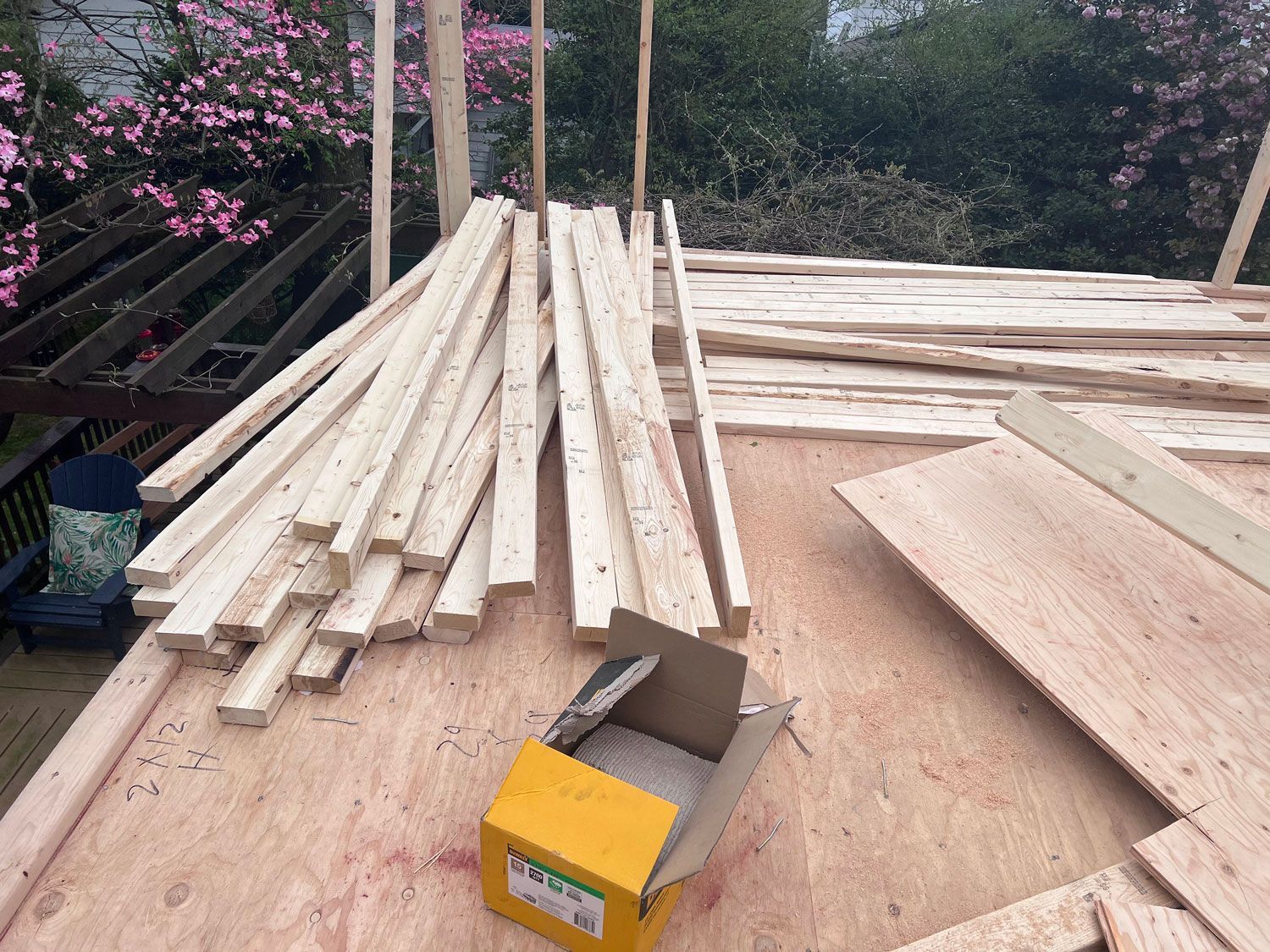 Wooden planks and plywood boards on a construction site, with a box cutter, trees in the background.