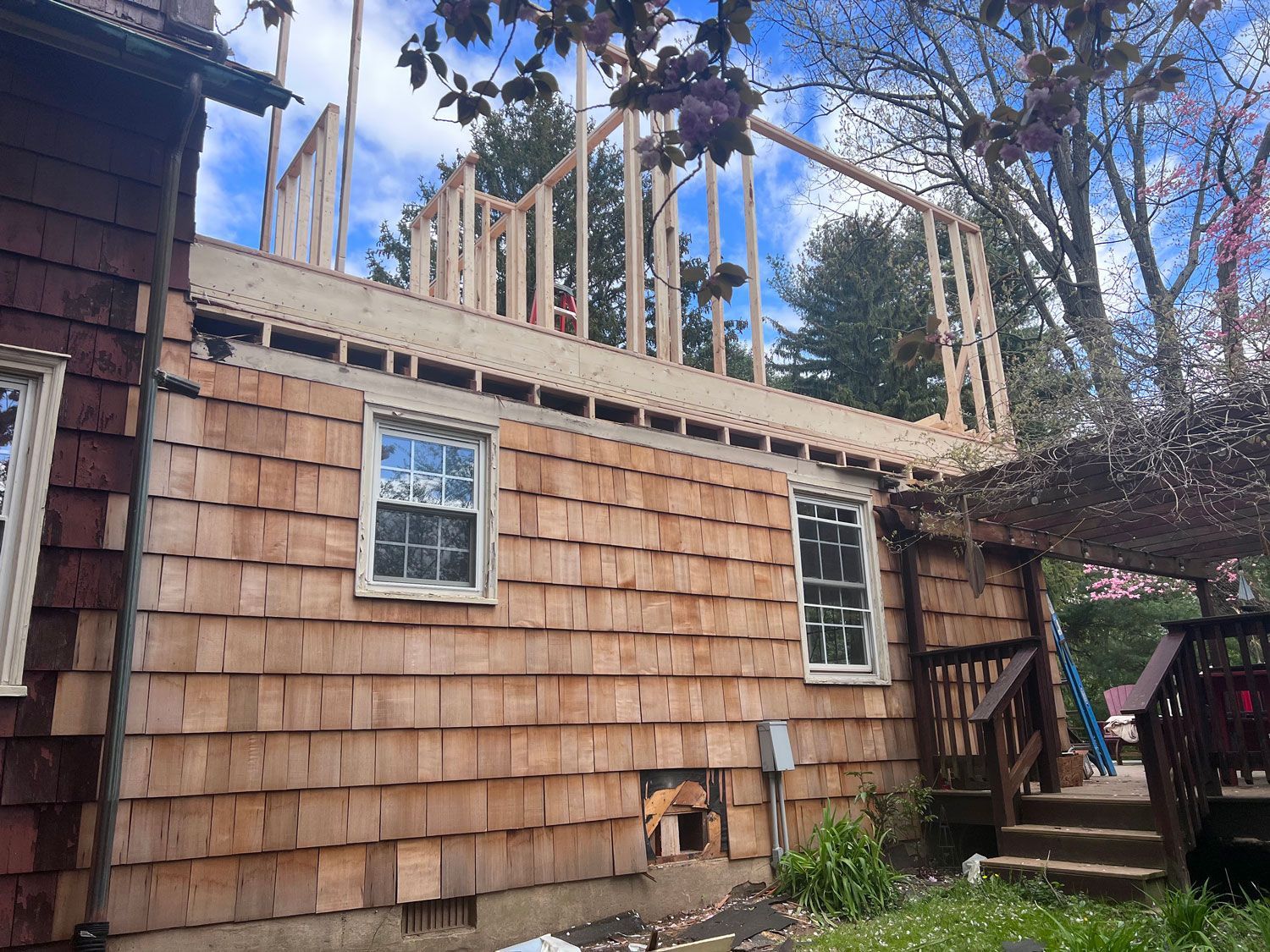 House undergoing renovation; wooden frame extension above the existing shingled roof; sunny outdoors.