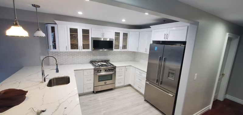 Modern, white kitchen with stainless steel appliances, white countertops, and wood floors.