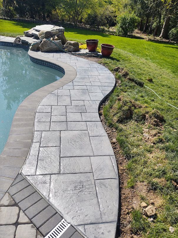 Stone pathway curves beside a pool and lawn; potted plants in background.