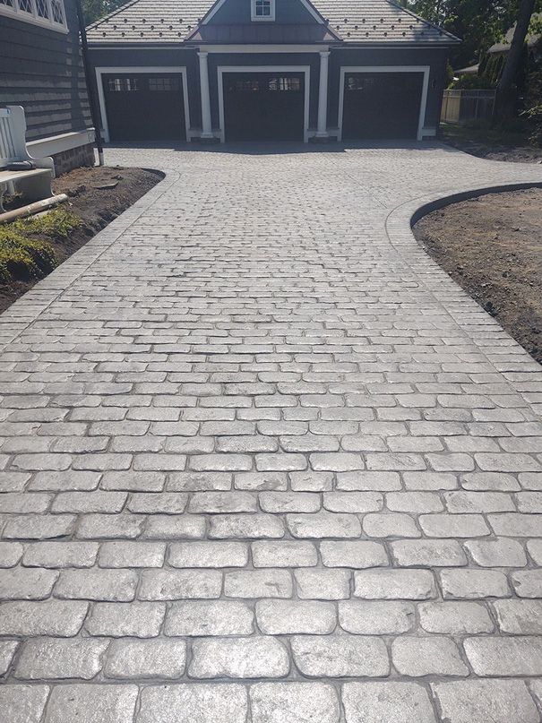 Gray brick-patterned concrete driveway leading to a garage with three dark doors.
