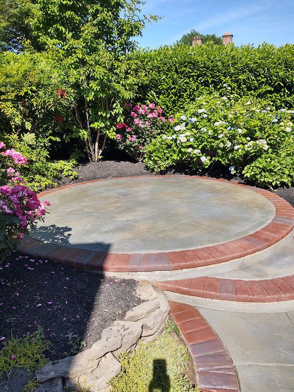 Circular stone patio with brick border surrounded by lush garden and flowers.
