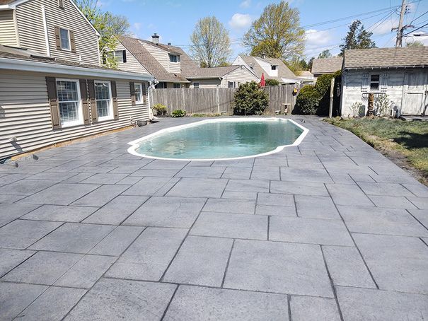 Gray concrete patio surrounds a blue oval pool; houses in the background.