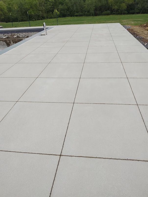 Large, light gray concrete patio with grid pattern next to a pool, ready for outdoor use.