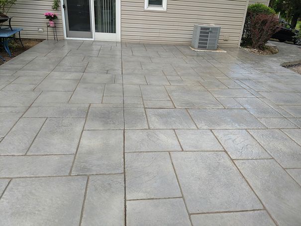 Gray stamped concrete patio outside a house with a sliding glass door.