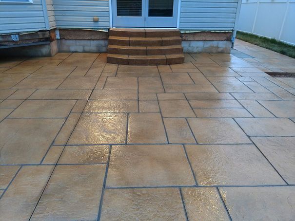 Brown concrete patio with textured rectangular patterns leading to a doorway with steps.