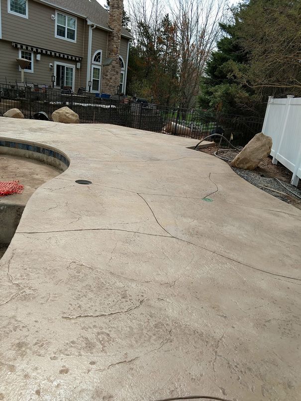 Concrete patio with cracks and a pool, leading to a house with a stone facade.