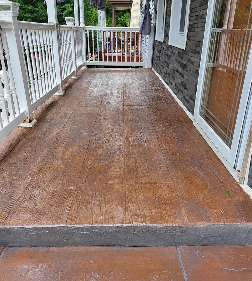 Brown, textured porch with a white railing. Dark stone wall, glass door, and gray step.