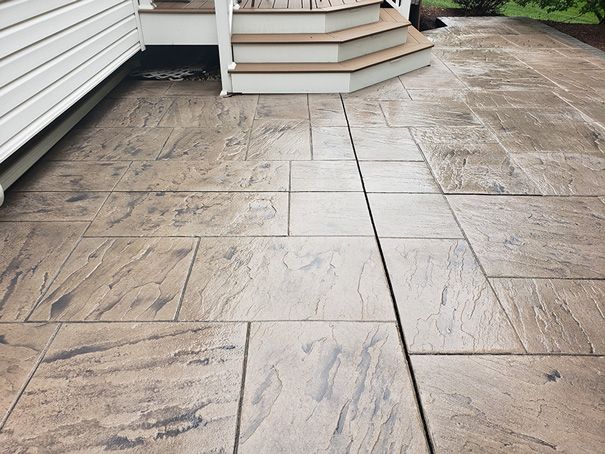 Stamped concrete patio with stairs leading up to a house. Light brown and gray hues.