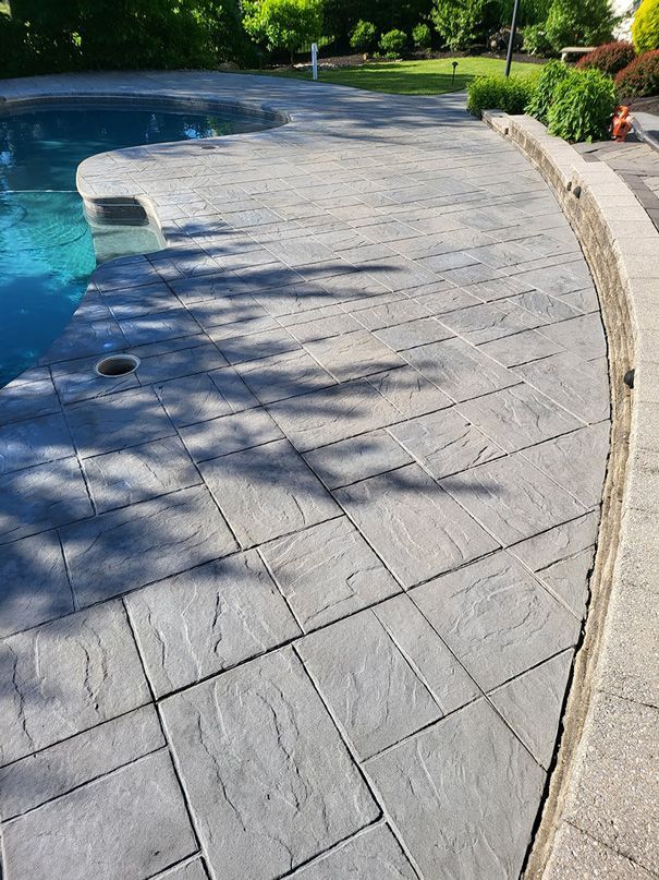 Grey stamped concrete pool deck with pool and curved border.
