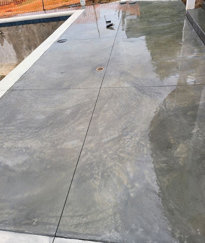 Wet, polished concrete patio beside a pool. Gray with lighter streaks.