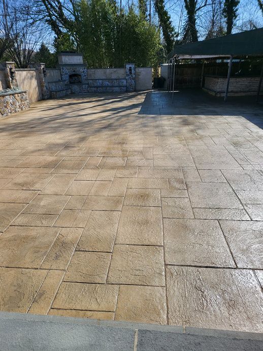 Stamped concrete patio with tan and brown tones. In the background are a stone wall, trees, and a gazebo.