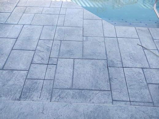 Gray stamped concrete patio bordering a pool.
