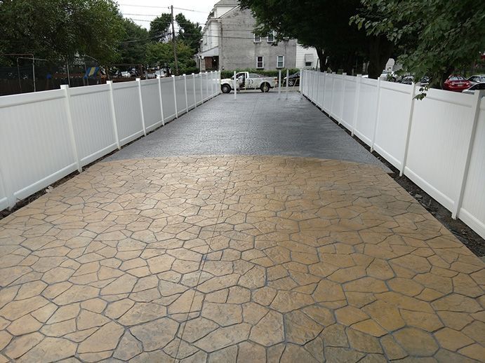 Long driveway lined with white fences, textured concrete surface.