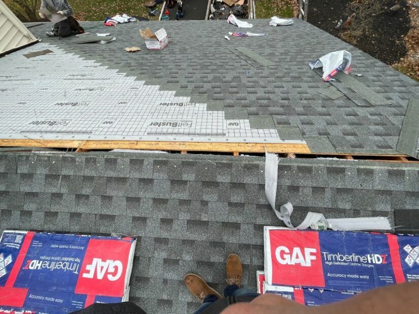 Rooftop with GAF shingles; partially installed. White underlayment visible. Brown shoes, debris, and tools scattered.