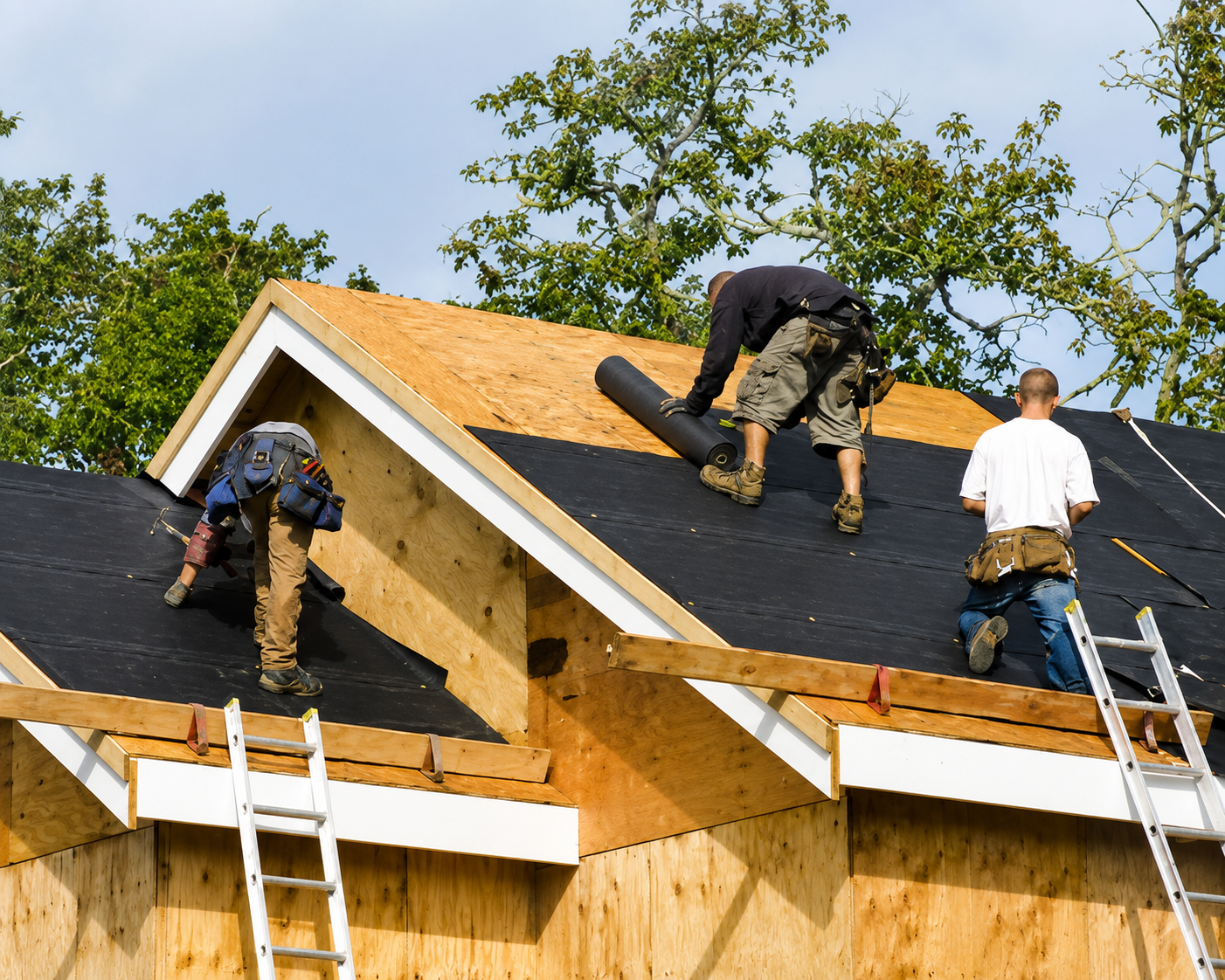 Three workers installing black roofing on a wooden house frame under construction