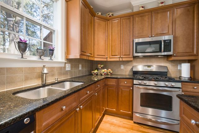 Kitchen with wooden cabinets, stainless steel appliances, black countertop, and a window.