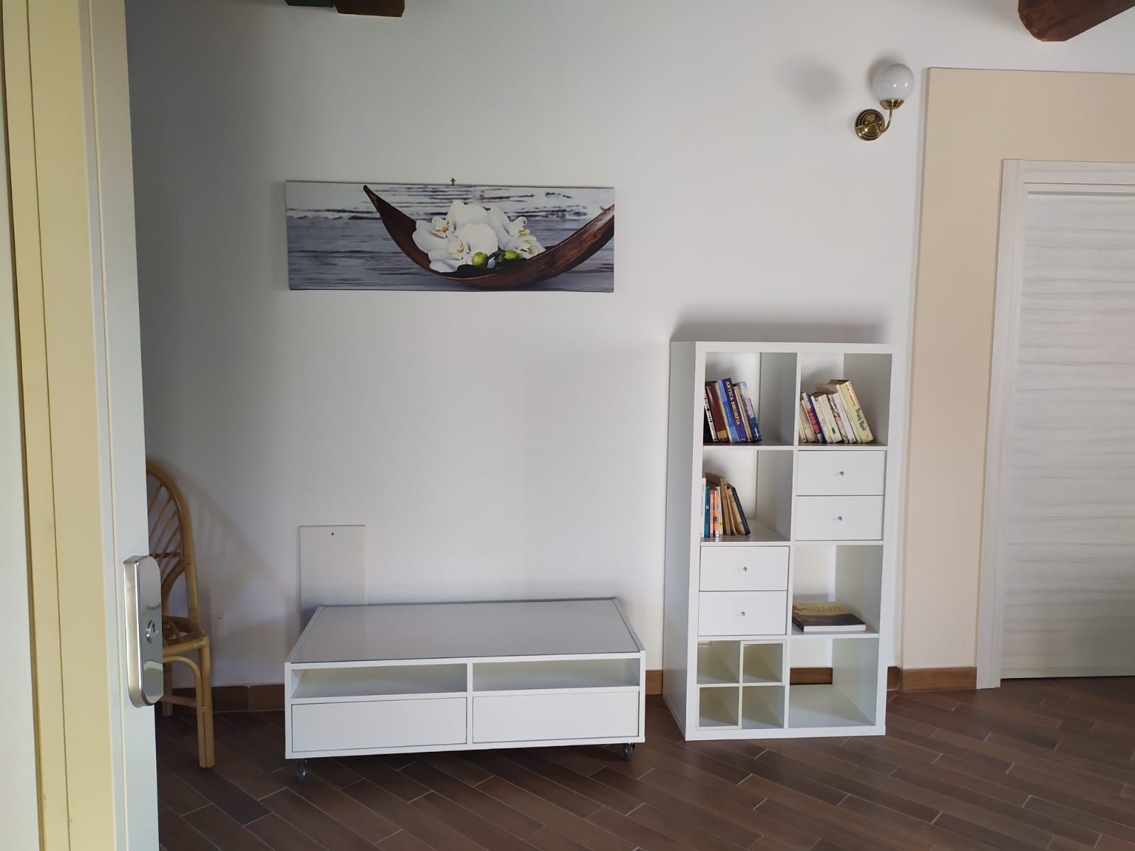 Mobili bianchi contro una parete bianca con un'opera d'arte floreale. Pavimento in legno.