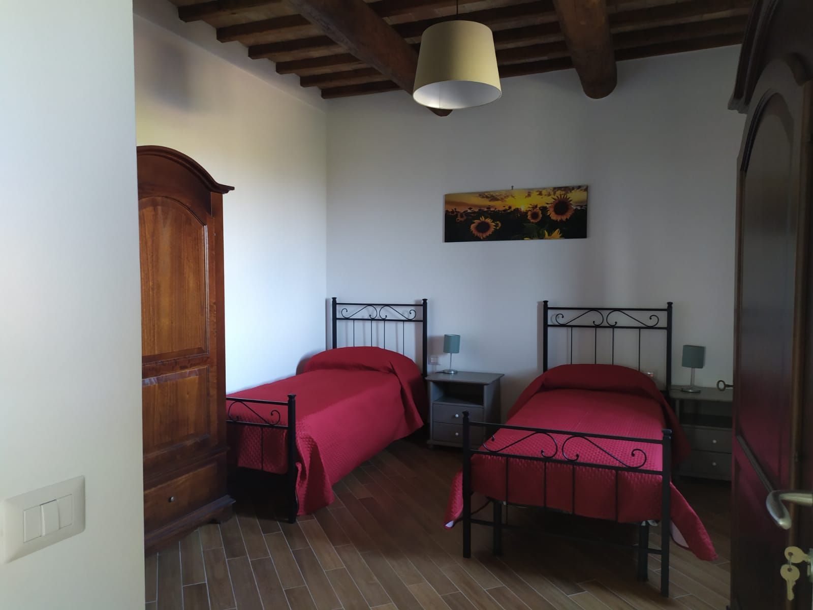 Camera da letto con due letti singoli, biancheria da letto rossa, mobili in legno scuro e un dipinto di girasoli.
