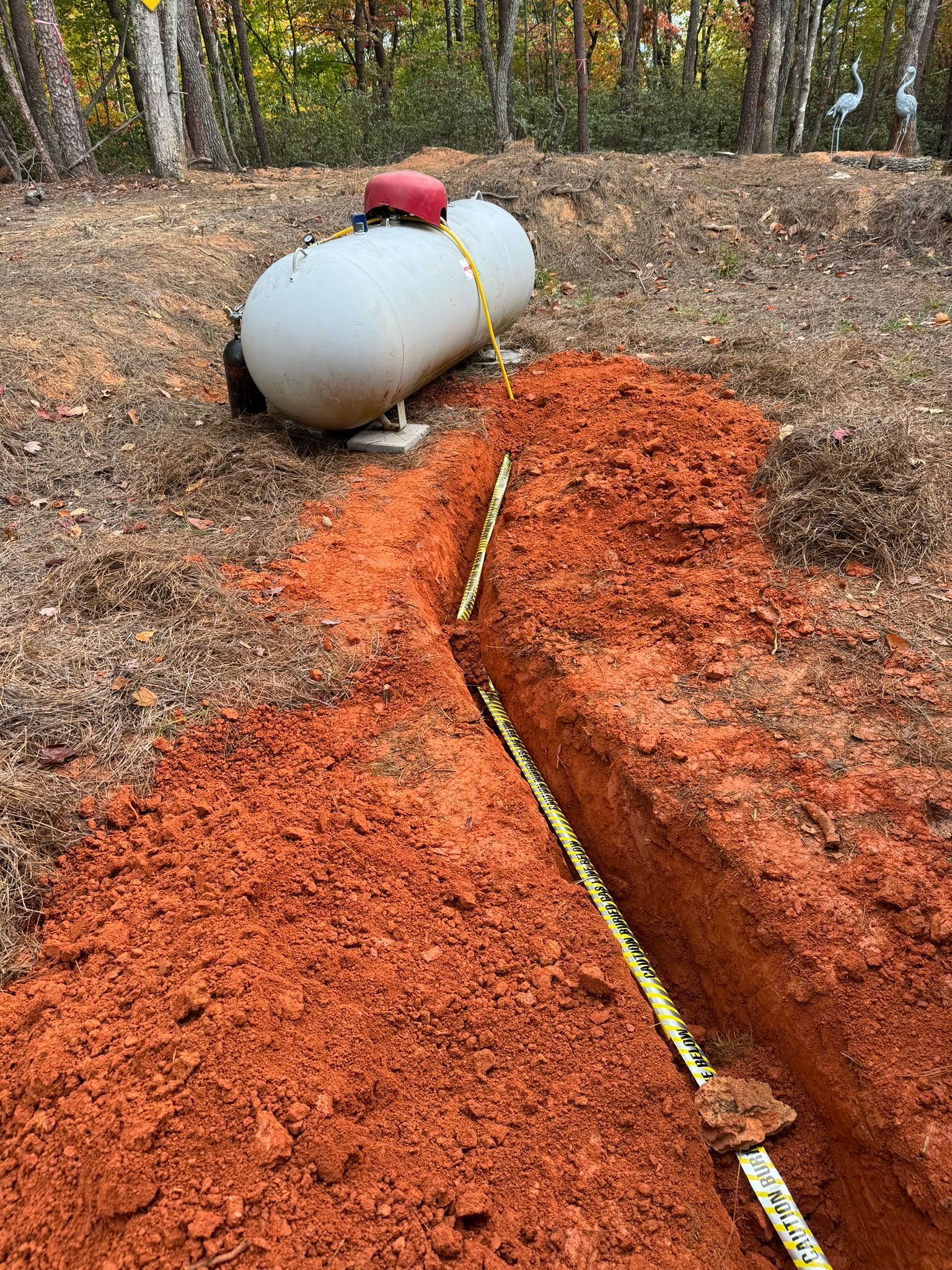 A propane tank is sitting in the dirt next to a measuring tape.