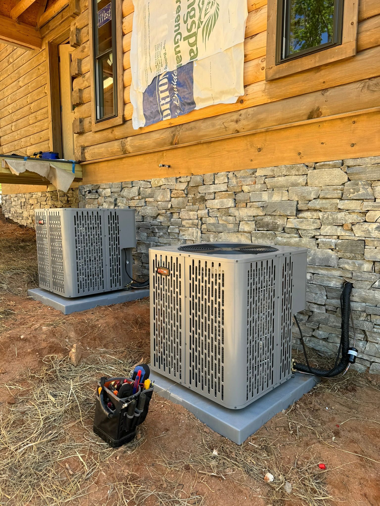 Two air conditioners are sitting on the side of a log cabin.