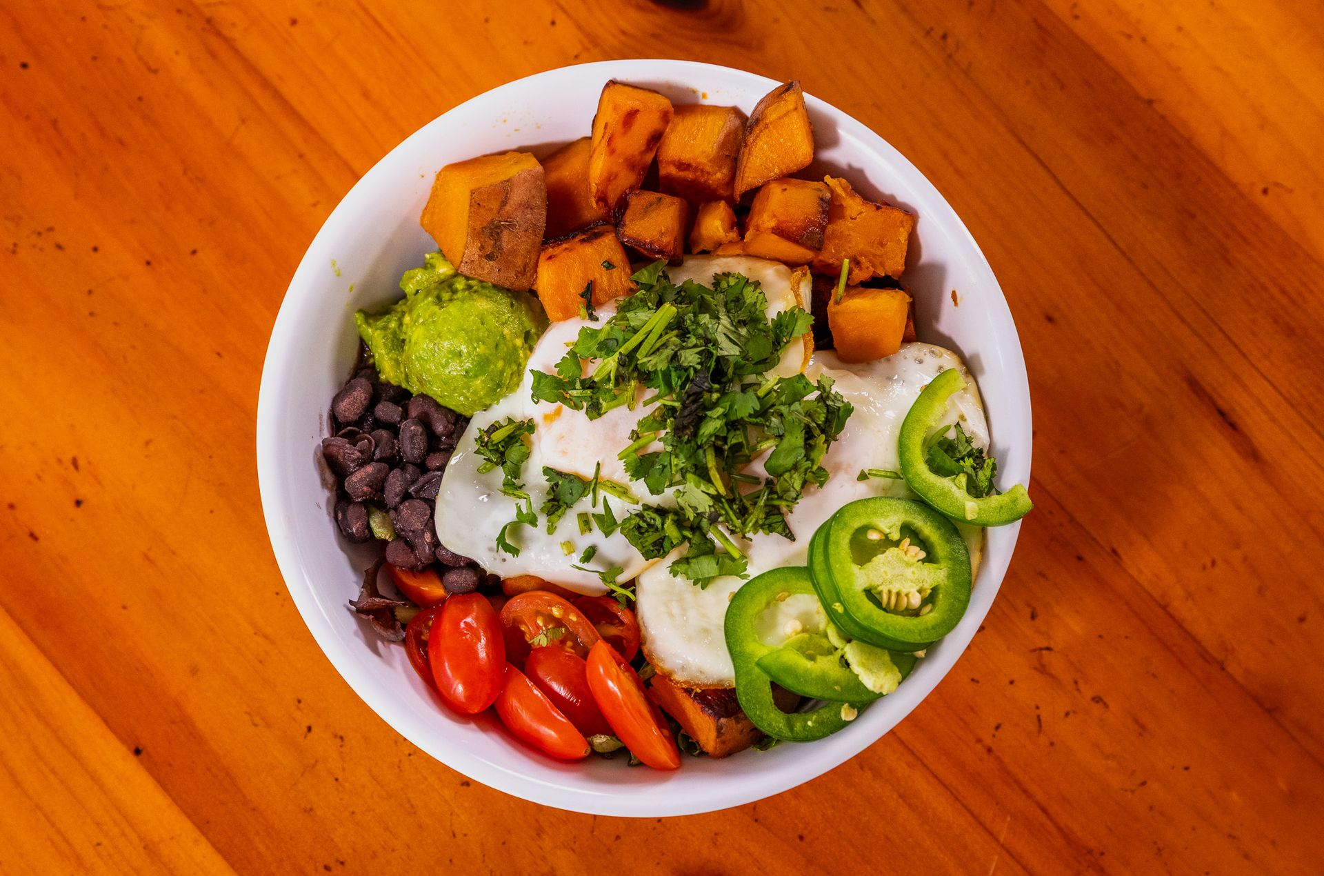Breakfast bowl with eggs, sweet potatoes, avocado, beans, tomatoes, and jalapenos.