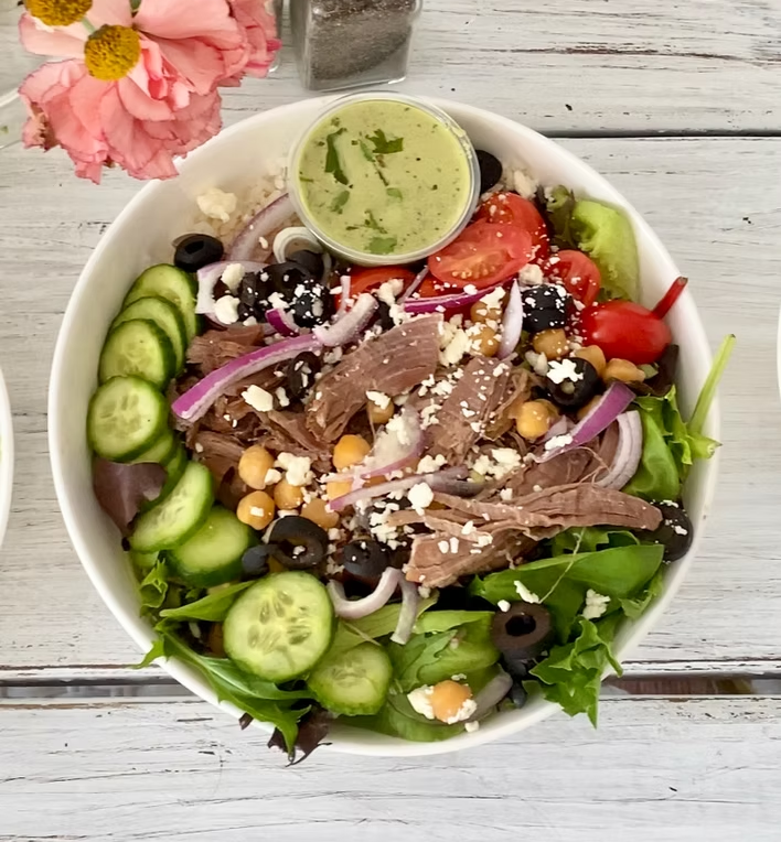 Greek salad with meat, olives, feta, and creamy dressing in a white bowl.