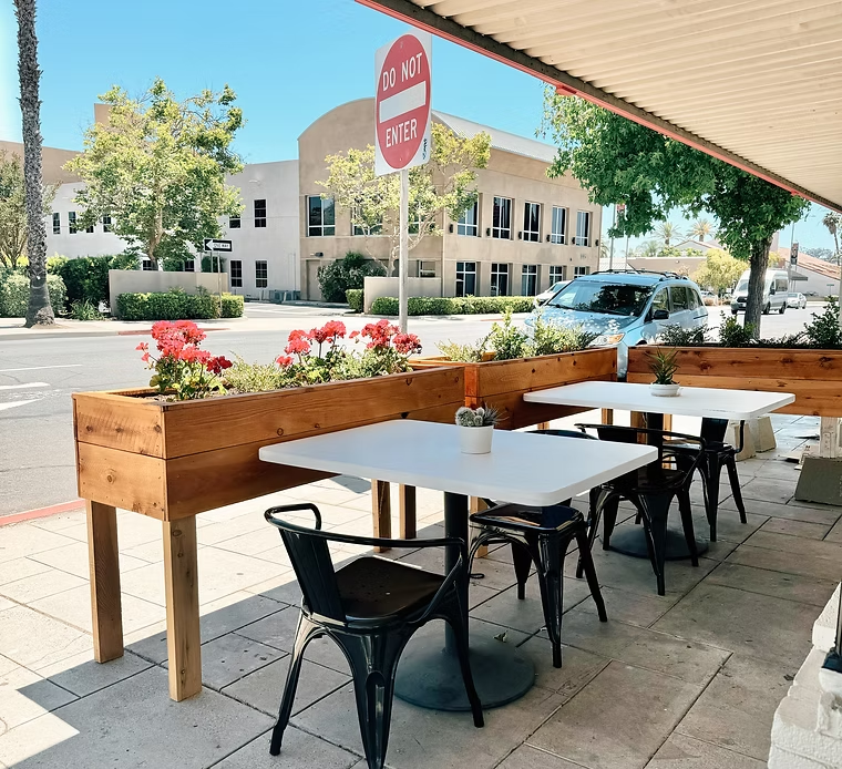 Outdoor cafe with tables and chairs, wooden flower box, red flowers, street view.