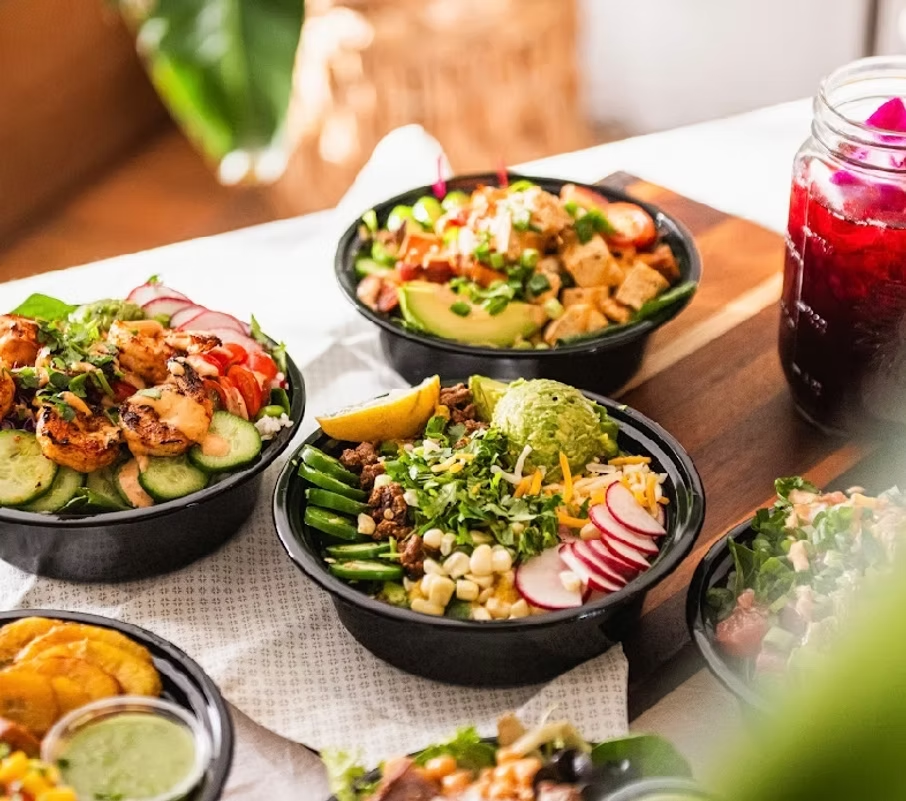 Bowls of colorful food: shrimp, tofu, and salad, with a drink, on a table.